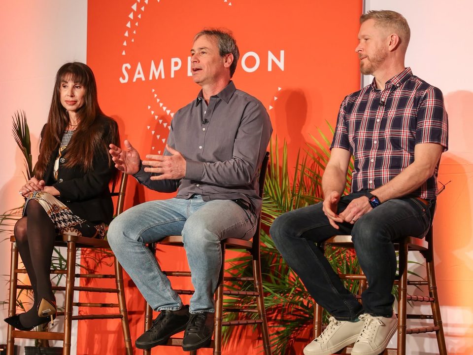 Terry Sweeney seated on stage with fellow panelists in front of the SampleCon backdrop